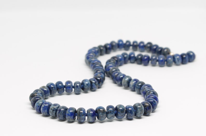 May include: A long necklace made of dark blue lapis lazuli beads. The beads are round and have a slightly irregular shape. The necklace is strung on a thin cord.