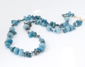 May include: A long necklace made of blue and green gemstone beads. The beads are irregular in shape and size, and they are strung on a thin gold chain.