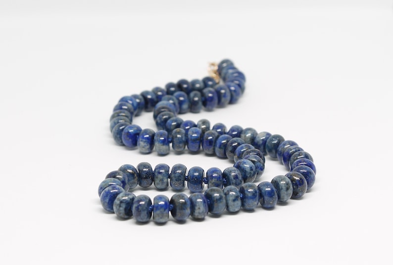 May include: A necklace made of dark blue lapis lazuli beads. The beads are round and have a slightly irregular shape. The necklace is strung on a thin gold chain.