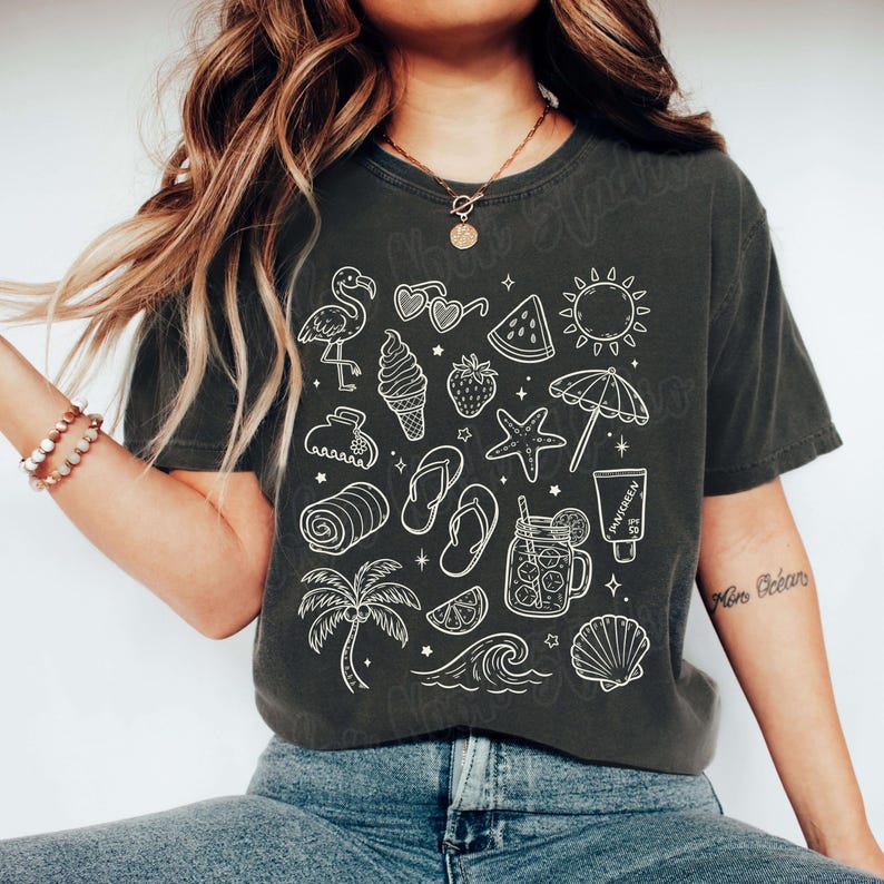 May include: A dark gray t-shirt with a white graphic print of various summer-themed icons, including a flamingo, sunglasses, watermelon, ice cream cone, a starfish, a palm tree, and a seashell.