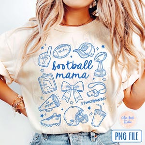 Puede incluir: Una camiseta blanca con un diseño gráfico azul que dice "football mama". El gráfico incluye un balón de fútbol, un silbato, un lazo de animadora, un casco de fútbol, un trofeo, un megáfono, un diagrama de jugada de fútbol y la mano de un jugador de fútbol haciendo un signo de número uno.