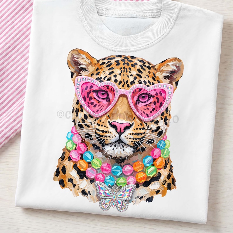 May include: A white t-shirt featuring a graphic illustration of a leopard wearing pink heart-shaped sunglasses with rhinestones, a multi-colored beaded necklace, and a large, iridescent butterfly pendant hanging from the center of the necklace.