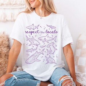 May include: White t-shirt with a purple graphic of various sharks and the text "Respect the Locals".