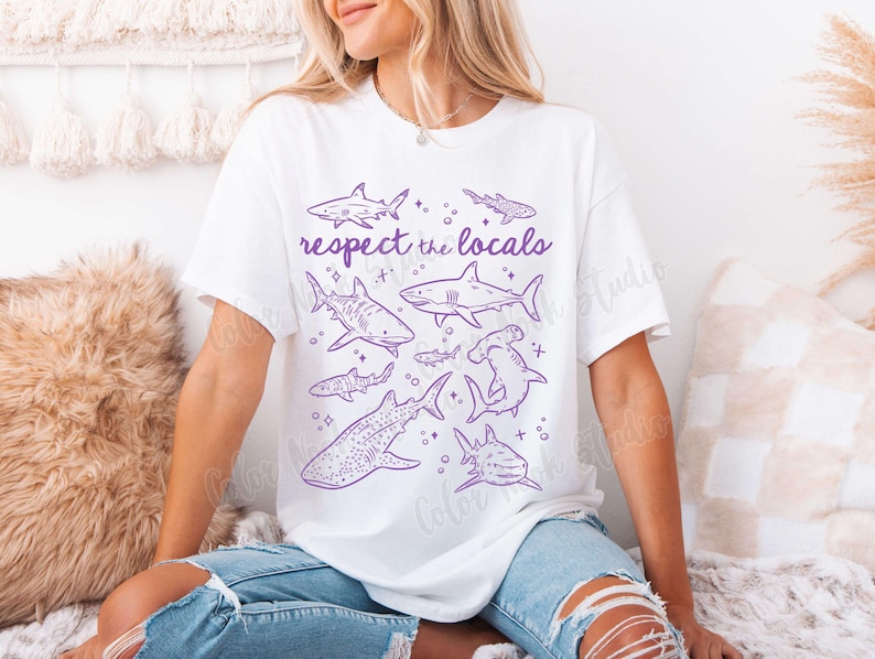 May include: White t-shirt with a purple graphic of various sharks and the text "Respect the Locals".