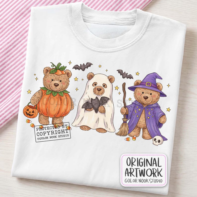 Op de afbeelding: Een wit t-shirt met een afbeelding van drie bruine teddyberen verkleed voor Halloween. E&eacute;n beer draagt een pompoenkostuum, &eacute;&eacute;n is een geest die een vleermuis vasthoudt en &eacute;&eacute;n is een tovenaar met een paarse mantel en hoed. Kleine vleermuizen en sterren.