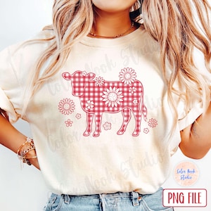 May include: Cream-colored t-shirt featuring a red gingham cow design with floral accents. The cow silhouette is filled with a red and white checkered pattern and surrounded by flower illustrations. The words "PNG FILE" are in the bottom right corner.