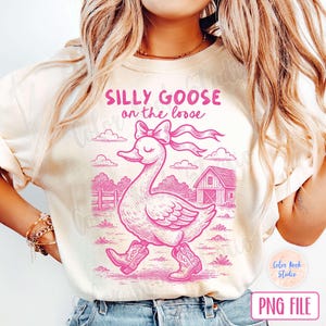 Op de afbeelding: Een wit T-shirt met een roze afbeelding van een gans met een roze strik en de tekst "Silly Goose on the Loose".