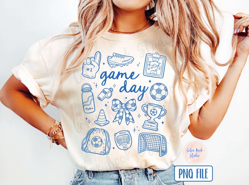 May include: A white t-shirt with a blue graphic design that says "game day" and features various sports-related icons, including a football, a whistle, a trophy, a football boot, and a water bottle.