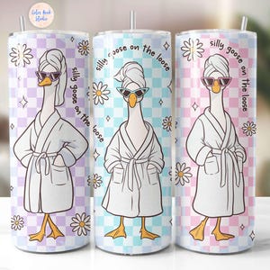 Pode incluir: Três copos de aço inoxidável com fundo xadrez rosa, azul e roxo. Cada copo apresenta um desenho animado de um ganso usando um roupão branco e óculos de sol com o texto "silly goose on the loose" impresso no lado.
