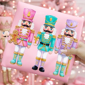 May include: Three colorful nutcracker figures on a pink background. The nutcrackers are in pink, teal, and purple, each with a different accessory. One holds a gingerbread man, another a gift, and the last a sword. The figures have white hair and mustaches.