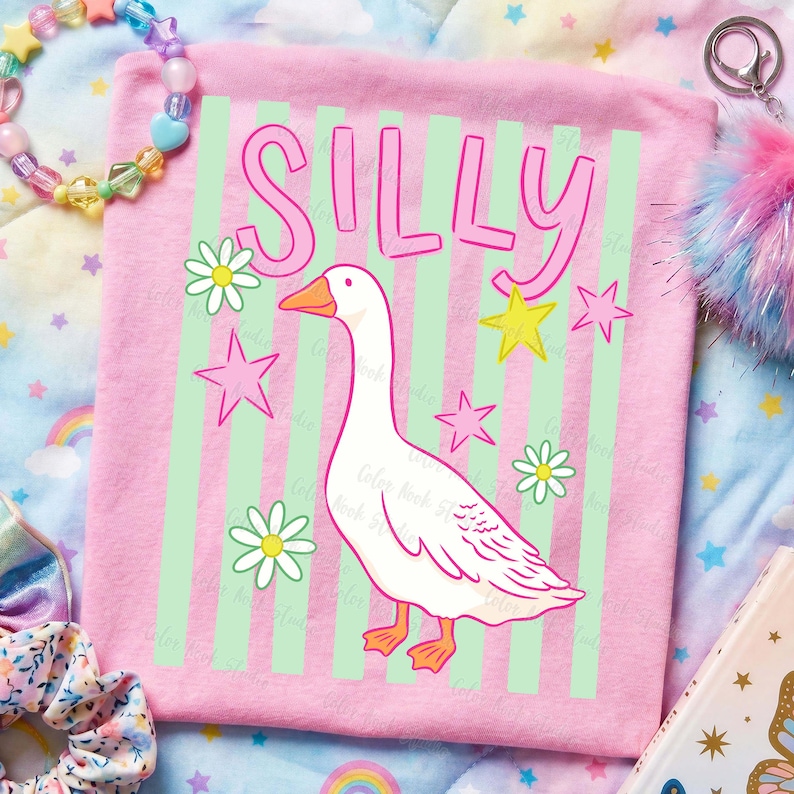 May include: Pink t-shirt with the word "SILLY" in pink letters above a white goose illustration. The shirt has green vertical stripes and is decorated with pink stars and white daisies.