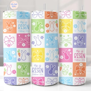 May include: Three stainless steel tumblers with a white background and a colorful pattern of bows, bunnies, and carrots. The tumblers have the text "He is Risen" and "Matthew 28:6" printed on them.