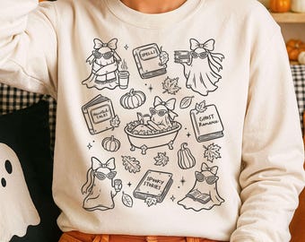 Könnte beinhalten: Cremefarbenes Sweatshirt mit einem schwarz-weißen Halloween-Motiv. Das Design zeigt Geisterfiguren mit Sonnenbrillen und Schleifen, umgeben von Büchern mit Titeln wie "Spells" und "Spooky Stories", Kürbissen und Herbstblättern.
