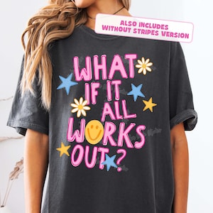 May include: Dark gray t-shirt with the phrase "WHAT IF IT ALL WORKS OUT?" in pink, outlined in white. The design includes blue stars, yellow stars, and daisy flowers. The shirt also includes a smiley face.