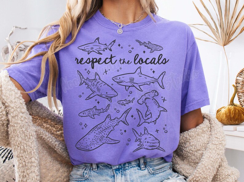May include: Purple t-shirt with a graphic of various sharks and the text "respect the locals".