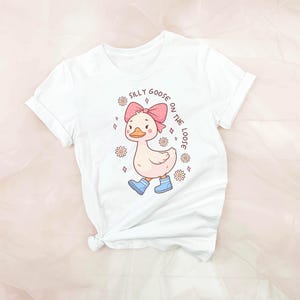May include: White t-shirt with a cartoon goose wearing a pink bow and blue rain boots. The text "Silly Goose on the Loose" is printed on the shirt.