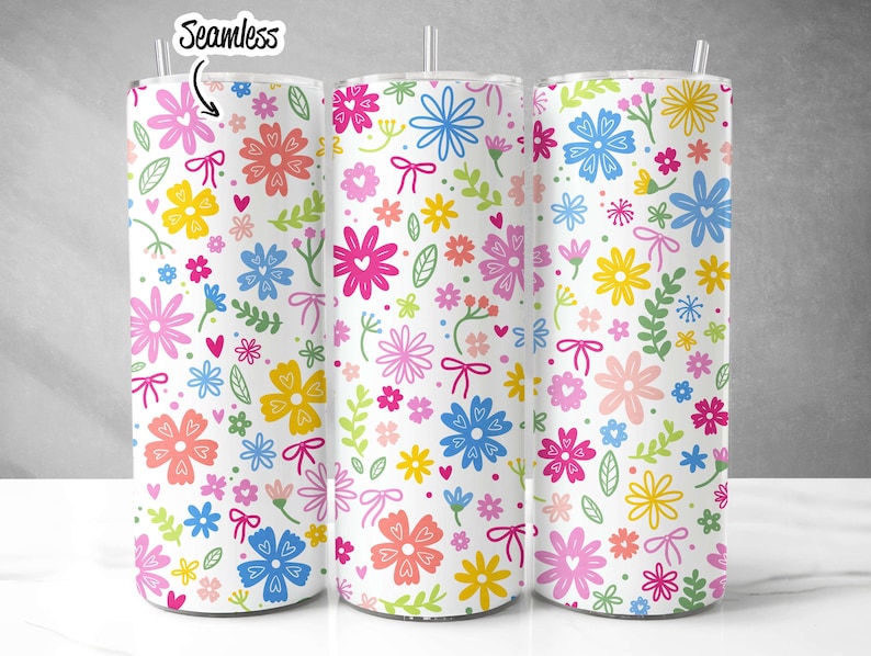 May include: Three stainless steel tumblers with a white background and a colorful floral pattern. The pattern includes pink, blue, yellow, green, and orange flowers with hearts and bows.