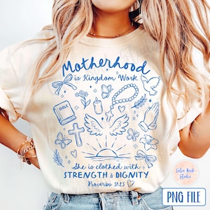 May include: A white t-shirt with a blue design that says "Motherhood is Kingdom Work" and includes various religious symbols like a dove, a cross, a bible, and a rosary. The design also includes the text "She is clothed with STRENGTH & DIGNITY Proverbs 31:25".
