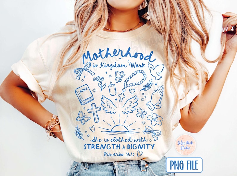 May include: A white t-shirt with a blue design that says "Motherhood is Kingdom Work" and includes various religious symbols like a dove, a cross, a bible, and a rosary. The design also includes the text "She is clothed with STRENGTH & DIGNITY Proverbs 31:25".