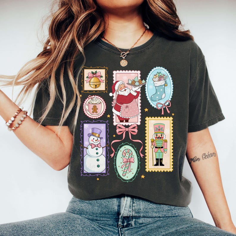 May include: Dark gray t-shirt featuring a collage of Christmas-themed illustrations. The design includes images of Santa Claus, a snowman, a bell, a stocking, a gingerbread man, a candy cane, and a nutcracker, all in a vintage stamp style.