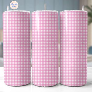 May include: Three tall, cylindrical tumblers with a pink and white gingham pattern. Each tumbler has a white straw and a lid. The tumblers are displayed on a white surface, with a blurred background featuring a bed and a plant.