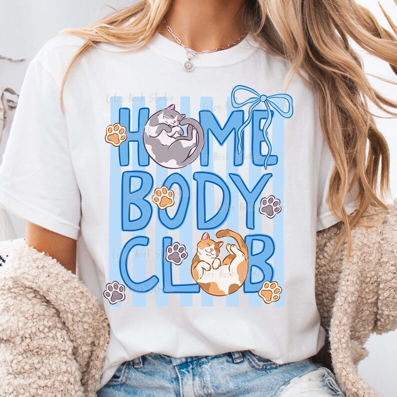May include: White t-shirt with a blue and white striped design and the words "HOME BODY CLUB" in blue. The shirt features illustrations of cats and paw prints.