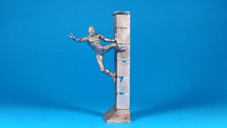 K&ouml;nnte beinhalten: Eine silberne Figur eines Menschen, der eine Wand aus gestapelten Bl&ouml;cken erklimmt. Die Person befindet sich in einer dynamischen Pose mit einem ausgestreckten Bein und einem ausgestreckten Arm.