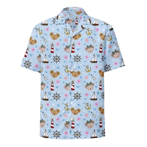 May include: Light blue button-down shirt with a nautical-themed pattern. The pattern includes teddy bears, lighthouses, sailboats, anchors, and ship wheels. The shirt has short sleeves and a classic collar.