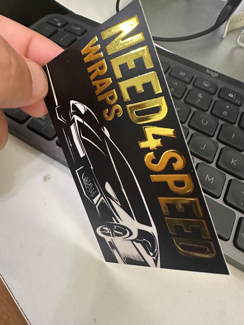 May include: Black and gold sticker with the text "NEED 4 SPEED WRAPS" in gold lettering. A black and white silhouette of a sports car is in the background.