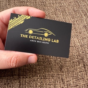 May include: Black business card with gold lettering and a gold car silhouette. The text reads "The Detailing Lab Auto Detailing".