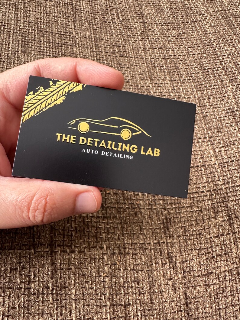 May include: Black business card with gold lettering and a gold car silhouette. The text reads "The Detailing Lab Auto Detailing".