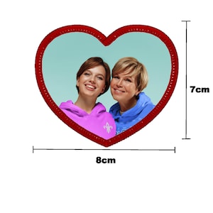 May include: Two people, a mother and daughter, smiling at the camera. They are wearing hoodies, one pink and one blue, and are framed in a red heart shape.