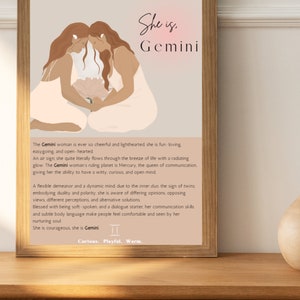 May include: A framed art print featuring a Gemini zodiac illustration. The artwork depicts two figures with flowing hair, holding a flower. The text "She is, Gemini" is at the top, with a description below. The print is displayed on a wooden surface.
