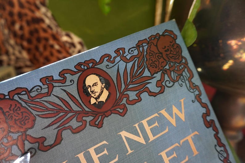 May include: A close-up of a book cover with the title "THE NEW FOLIO" in gold lettering. The cover is light blue with decorative brown illustrations, including a portrait of William Shakespeare.