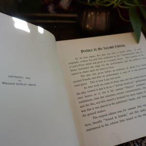 May include: An open book with text titled "Preface to the Second Edition." The page on the left reads "Copyright, 1915 by William Hawley Smith." The book is open on a table with a plant and vase in the background.