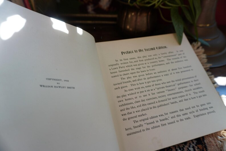May include: An open book with text titled "Preface to the Second Edition." The page on the left reads "Copyright, 1915 by William Hawley Smith." The book is open on a table with a plant and vase in the background.