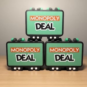 May include: Three green Monopoly Deal game cases stacked on a wooden surface. Each case has the words "MONOPOLY" in orange and "DEAL" in white. The cases have black and green accents.