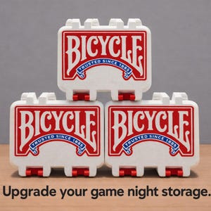 May include: Three white rectangular storage cases for playing cards, stacked in a pyramid formation. Each case features the red and white Bicycle logo with the text Trusted Since 1885. The text Upgrade your game night storage is below.