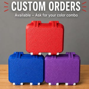 May include: Three rectangular storage cases with textured surfaces, stacked in a pyramid formation. The top case is red, the bottom left is blue, and the bottom right is purple. Each case features white latches. Text reads: CUSTOM ORDERS Available – Ask for your color combo.