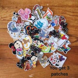 May include: A collection of embroidered patches featuring various cartoon characters and designs. The patches include Mickey Mouse, Minnie Mouse, Winnie the Pooh, and other Disney characters. The text "You get 3 patches" is visible.