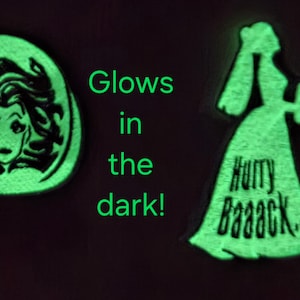 May include: Two glow-in-the-dark pins. One is an oval with a woman's face, the other is a silhouette of a woman in a dress holding a fan, with the text "Hurry Baaaack...". The text "Glows in the dark!" is also present.