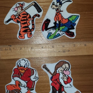 May include: Four embroidered iron-on patches featuring Disney characters playing sports. The patches are white with colorful embroidered images of a tiger holding a hockey stick, a dog on a surfboard, a duck holding a football, and a dwarf holding a hockey stick.