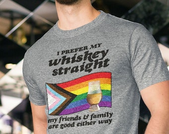 Può includere: Una maglietta grigia con il testo "I prefer my whiskey straight" e una bandiera arcobaleno con un bicchiere di whisky. Il testo "my friends & family are good either way" è sotto la bandiera. La maglietta è una Gildan 64000 Unisex Softstyle T Shirt. È inclusa una tabella delle taglie con le misure in pollici.