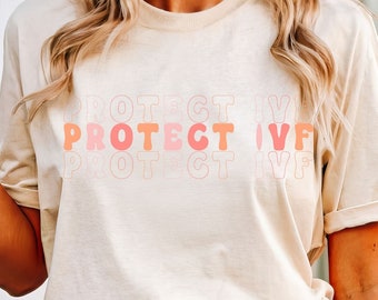 May include: Beige t-shirt with the words "PROTECT IVF" in a repeating pattern of orange and pink letters. The shirt is paired with light blue denim shorts. The overall style is casual and comfortable.