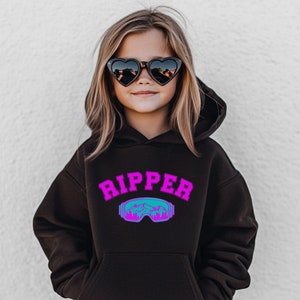 May include: A black hooded sweatshirt with a pink "RIPPER" graphic and a blue and green ski goggle design. The sweatshirt has a kangaroo pocket.