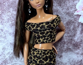 May include: A doll with long brown hair and dangling earrings is wearing a two-piece outfit. The outfit consists of a crop top and a mini skirt with a leopard print pattern in brown and black. The skirt has a black lace trim.