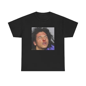 May include: A black t-shirt with a photo of a person's face with a bloody nose. The person has long, dark hair and is wearing a purple shirt.