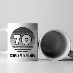 A white 11-ounce ceramic mug with a comfortable C-handle and rounded edges. The black and white design displays the words 70 Is Only 21 in Celsius.