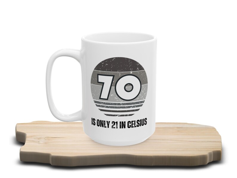 White ceramic mug on a wooden surface, featuring a vintage-style circular graphic with the number “70” and the text “Is only 21 in Celsius” in black lettering.