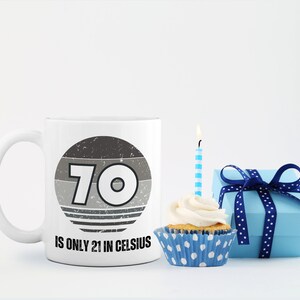 A white 11-ounce ceramic mug with a comfortable C-handle and rounded edges. The black and white design displays the words 70 Is Only 21 in Celsius.